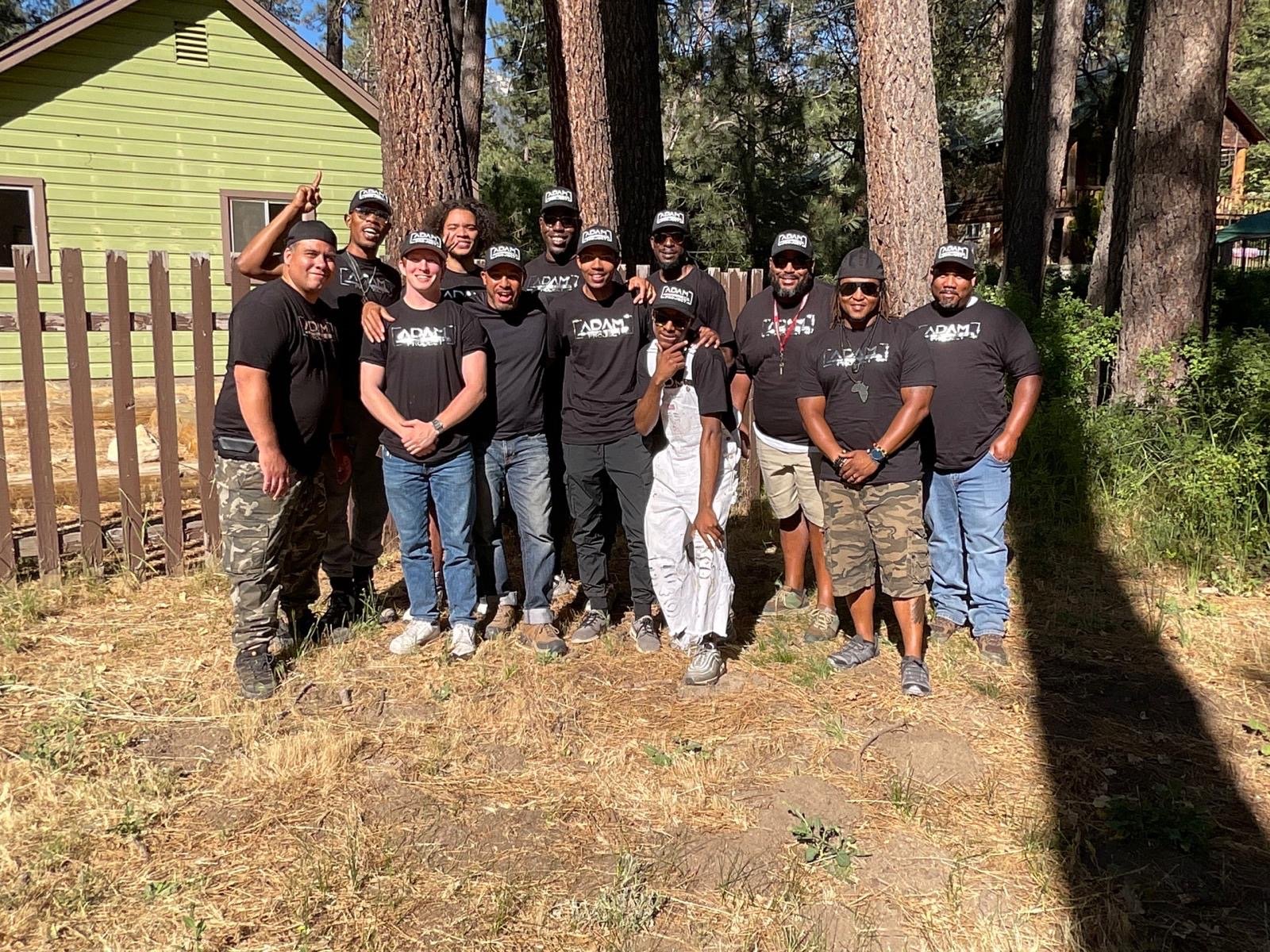 Men of The Adam Project in matching shirts posing together outdoors among pine trees