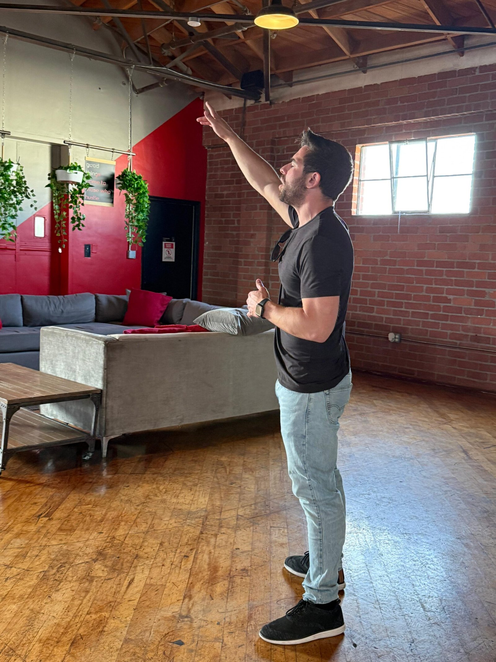 A man pointing upward while speaking in a brick-walled meeting space